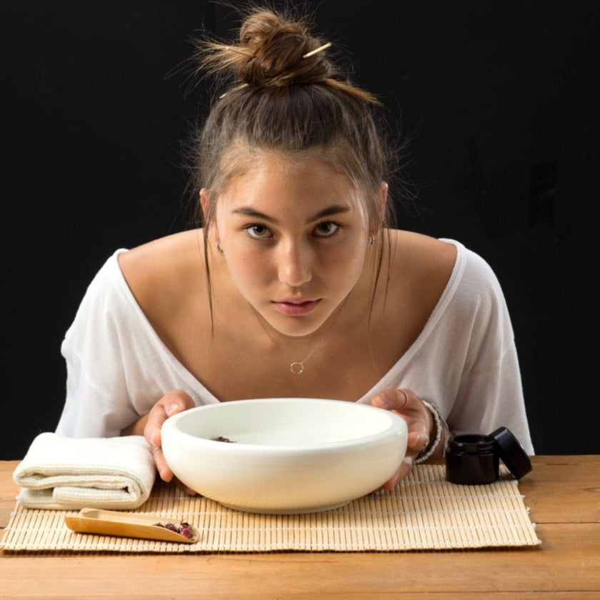 Beautiful young asian woman steaming her face over a bowl of hot tea
