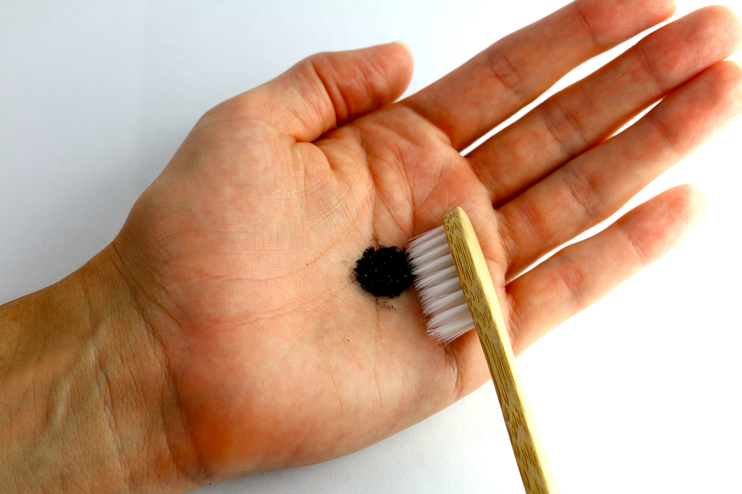 Pictured is Shen Blossom's Tooth Polish  in the palm of a person's hand being applied to a tooth brush.
