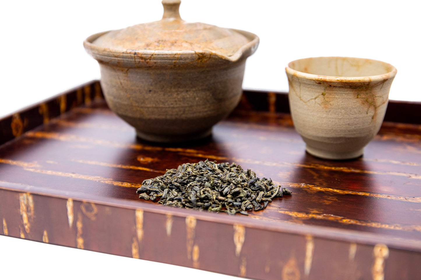 Pictured is a serving tray holding a teapot and cup next to a pile of aged Chrysanthemum and Jasmine Green Tea