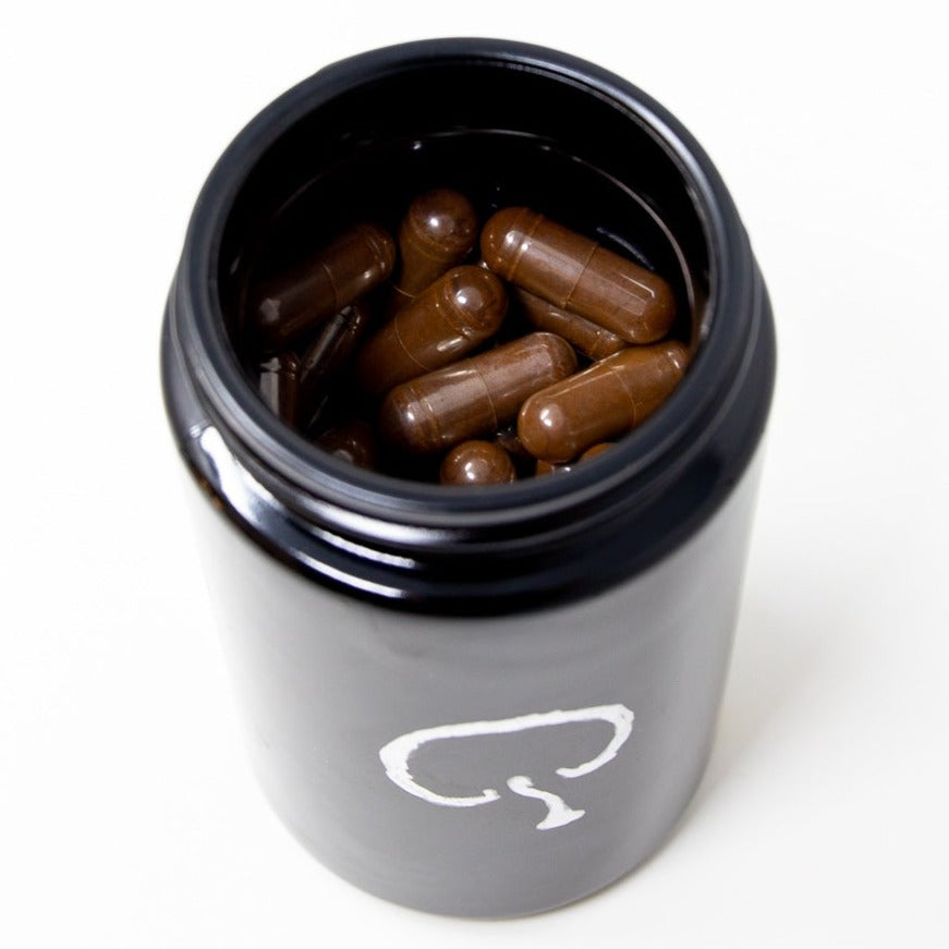 A jar showing the capsules inside of Shen Blossom's Wild Red Reishi Mushroom Full Spectrum Powder that's photographed on a white background
