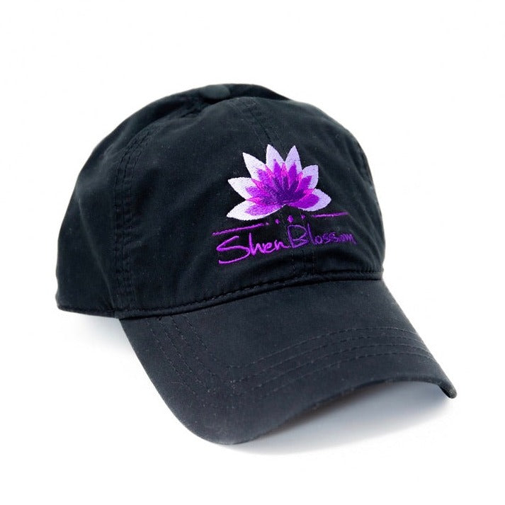 A black hat with purple Shen Blossom lotus logo pictured on a white background