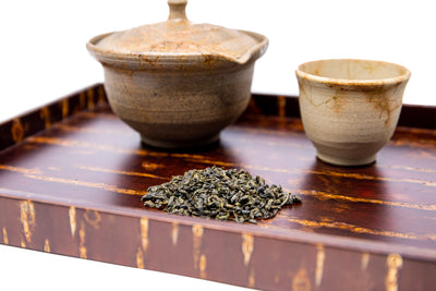 Pictured is a serving tray holding a teapot and cup next to a pile of aged Chrysanthemum and Jasmine Green Tea