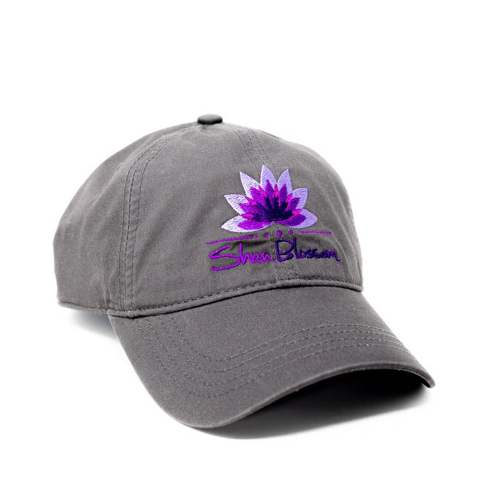 A charcoal hat with purple Shen Blossom lotus logo pictured on a white background 